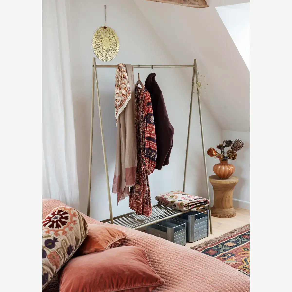 Madam Stoltz Velvet Cushion Covers in coral pink and embroidered patterns on a bed with a clothes rack.