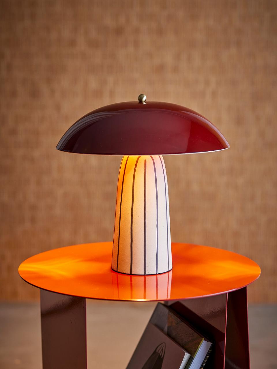 Arvid Stoneware Table Lamp by Bloomingville with red mushroom shade and striped base on an orange table.