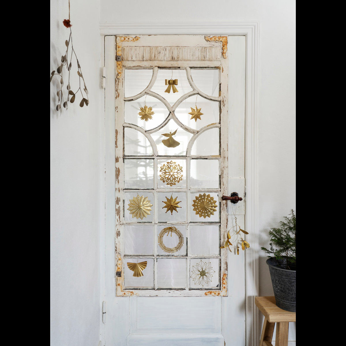 Madam Stoltz Hanging Brass Bow on a distressed white glass door with other gold Christmas decorations.