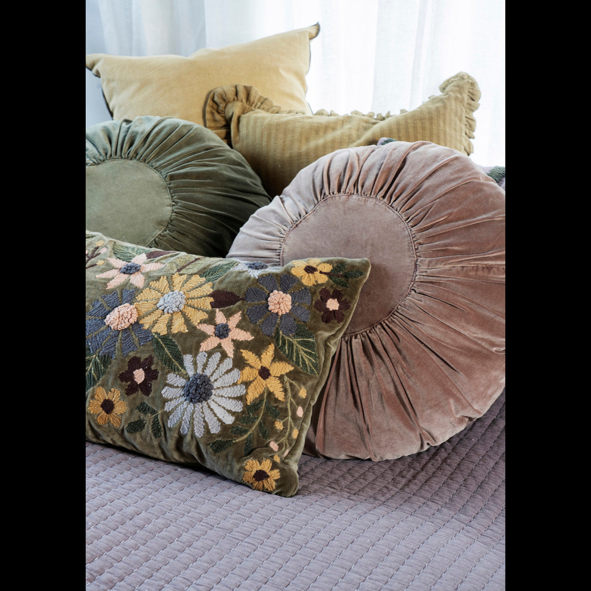 Madam Stoltz Round Velvet Cushion in dusty pink, surrounded by olive green velvet and floral embroidered cushions.