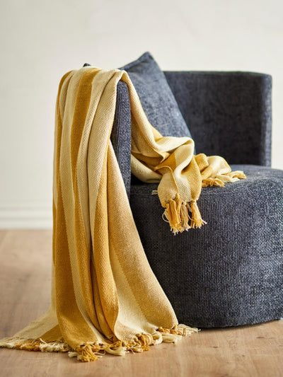 Frello Throw, Yellow | Bloomingville: Striped yellow and cream throw blanket with tassels draped over a dark gray armchair.