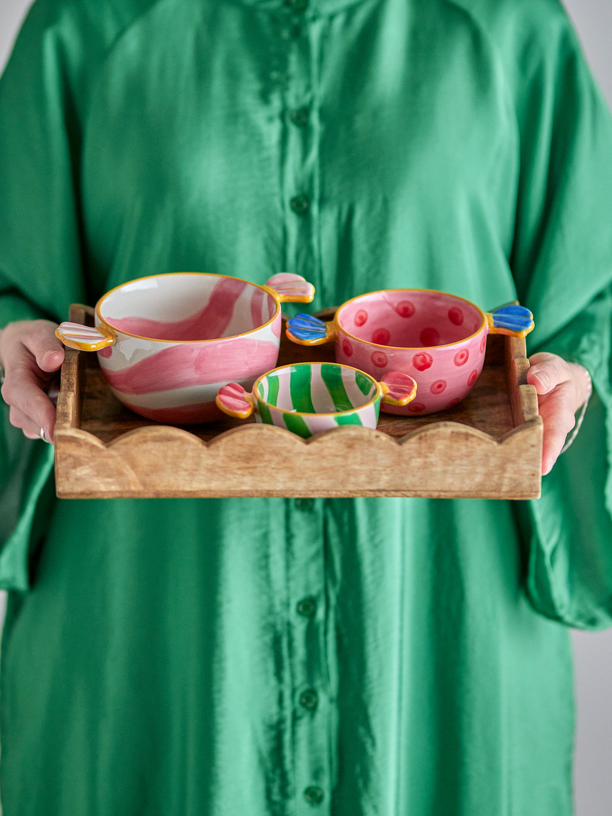 Bloomingville Caramella Bowl Set of 3, Multi. Person holds a wooden tray with three colorful, candy-handled bowls: pink stripes, pink polka dots, green stripes.