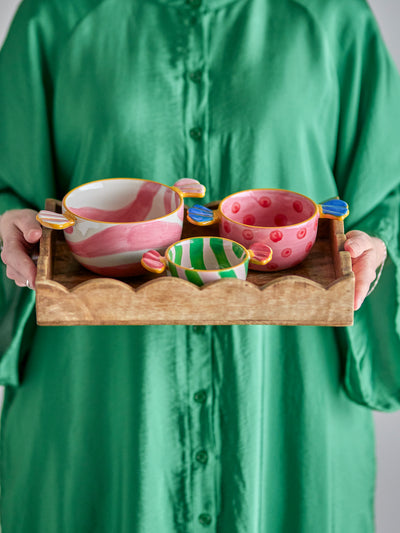 Bloomingville Caramella Bowl Set of 3, Multi. Person holds a wooden tray with three colorful, candy-handled bowls: pink stripes, pink polka dots, green stripes.