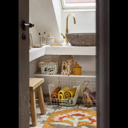 Oval Tufted Bath Mat by Madam Stoltz in a stylish, well-organized bathroom with a stone sink, golden faucet, and storage.