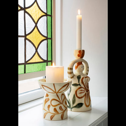 Hand-Painted Candle Holder Figurine by Madam Stoltz and a decorated pillar holder with lit candles on a sunny windowsill.