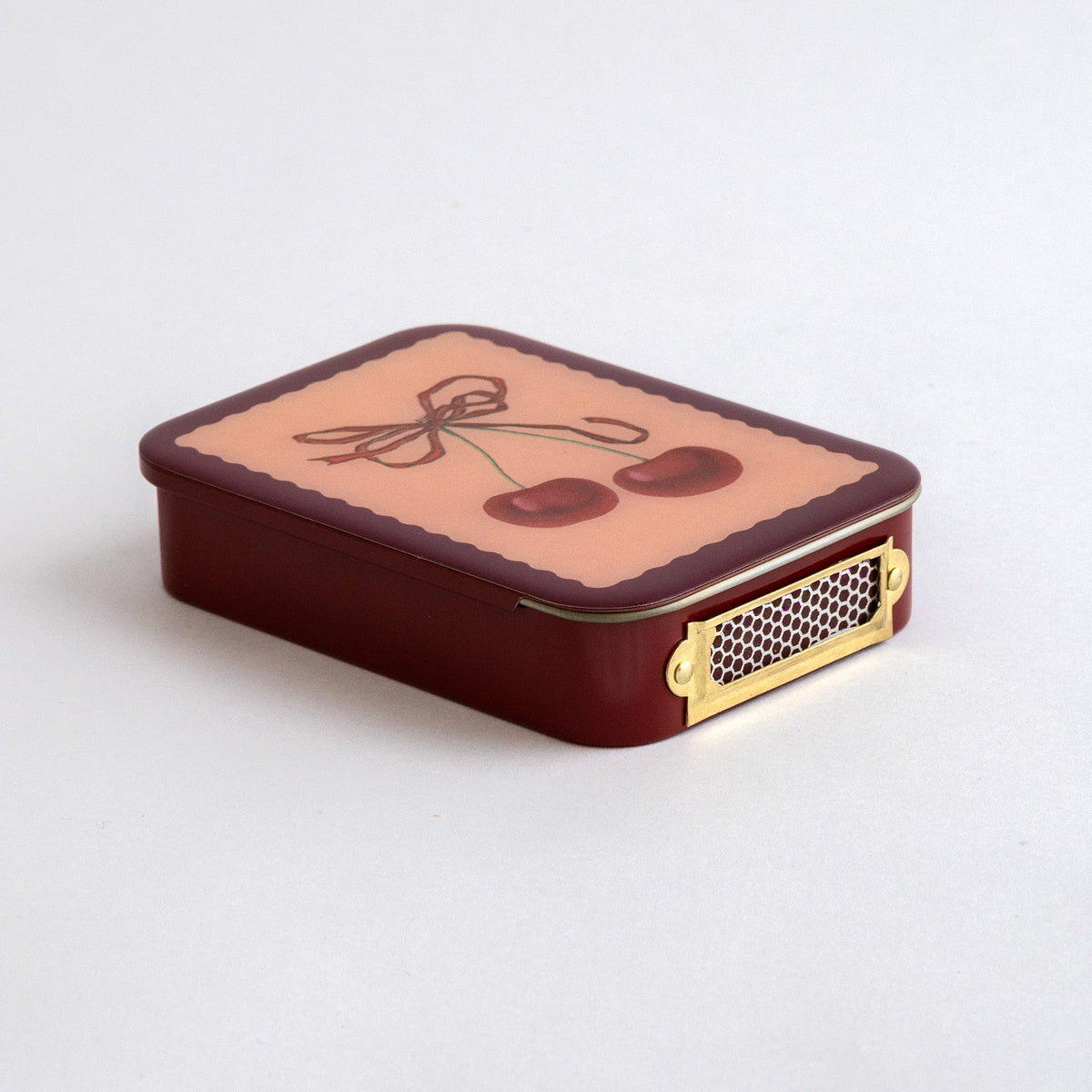 Roomytown Matches in Tin, dark red with a pink top featuring a cherry and bow illustration, brass strike plate