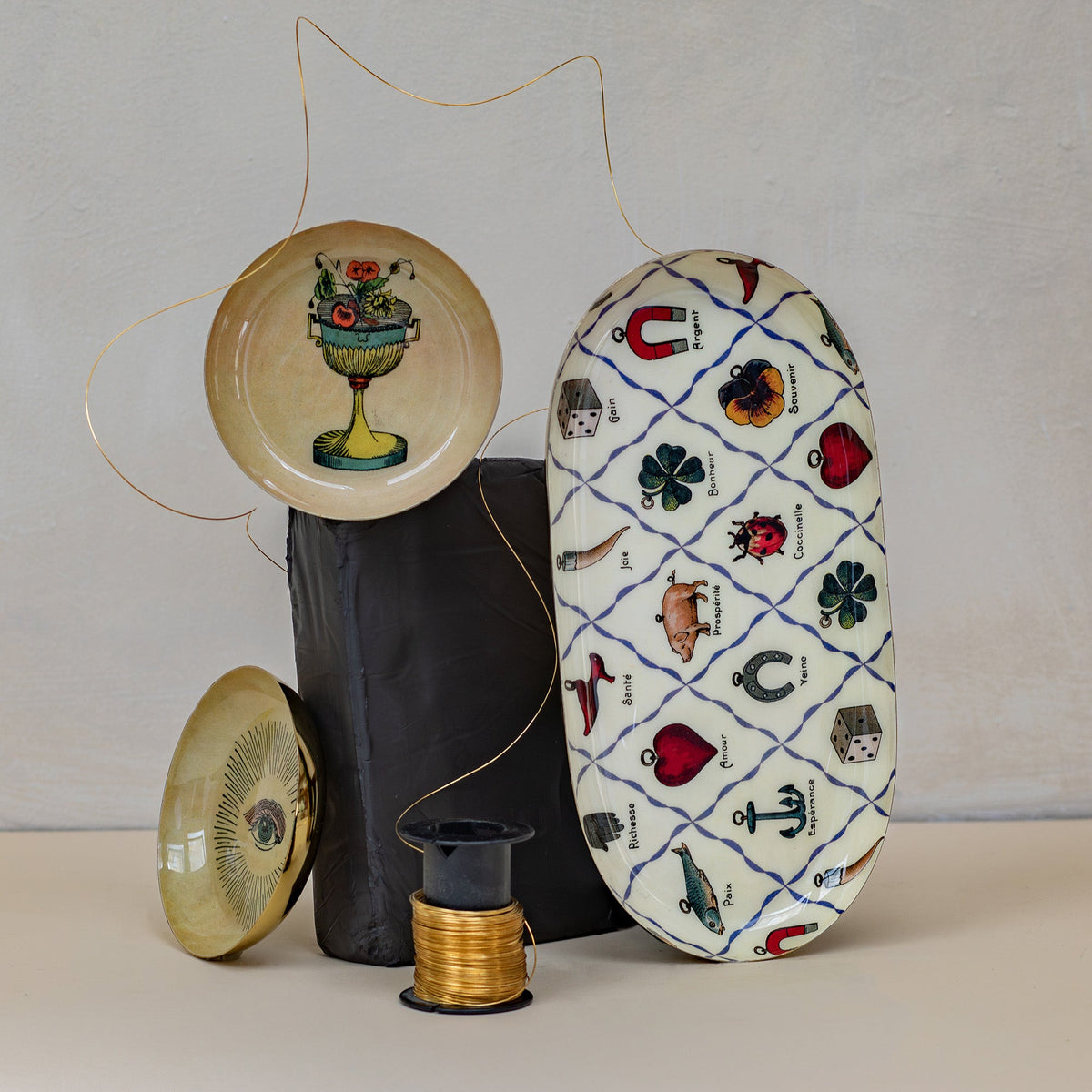 Roomytown Round Enamel Tray featuring a floral vase, alongside an oval tray with good luck charms &amp; gold wire.