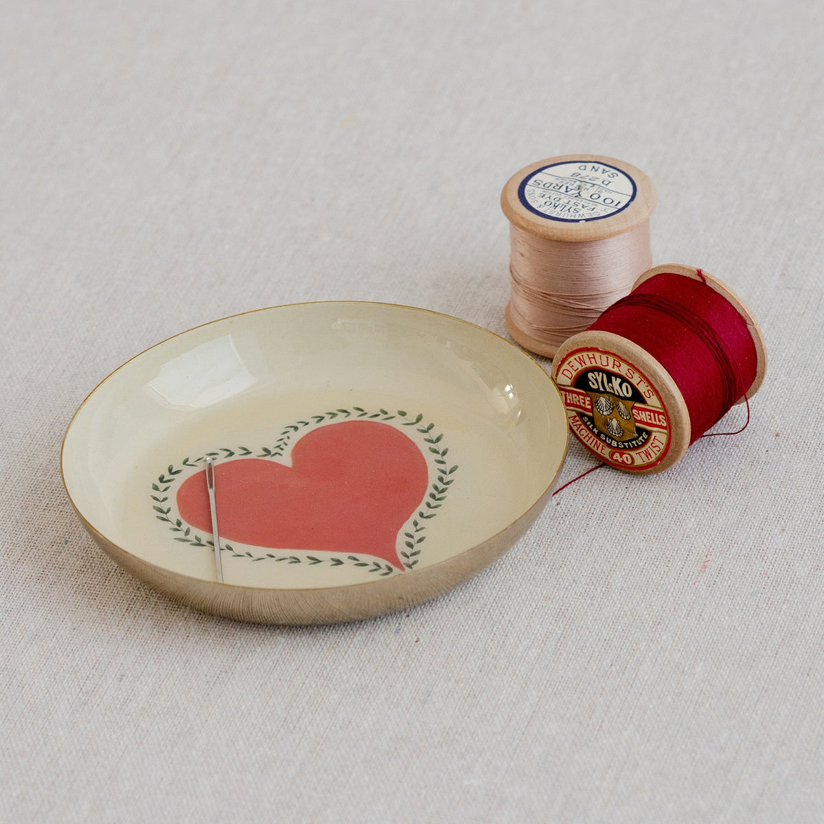Roomytown Round Enamel Tray featuring a red heart and needle, with vintage sewing thread spools on linen.