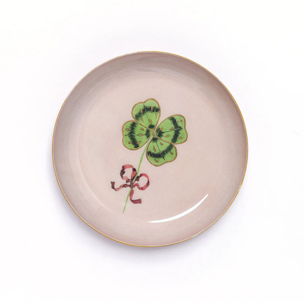 Round Enamel Tray by Roomytown with a vibrant green four-leaf clover and a red ribbon on a light pink background.