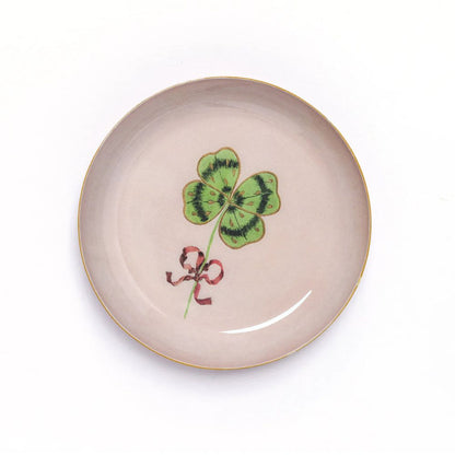 Round Enamel Tray by Roomytown with a vibrant green four-leaf clover and a red ribbon on a light pink background.