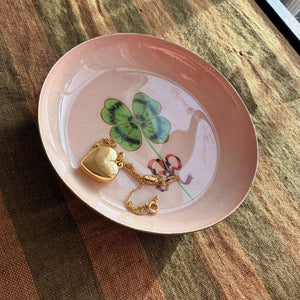 Round Enamel Tray by Roomytown in pink with a four-leaf clover design, holding a gold heart locket on a chain.
