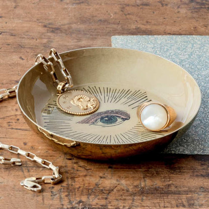 Round Enamel Tray | Roomytown featuring an eye design, holding gold ram pendant and pearl ring on wood.