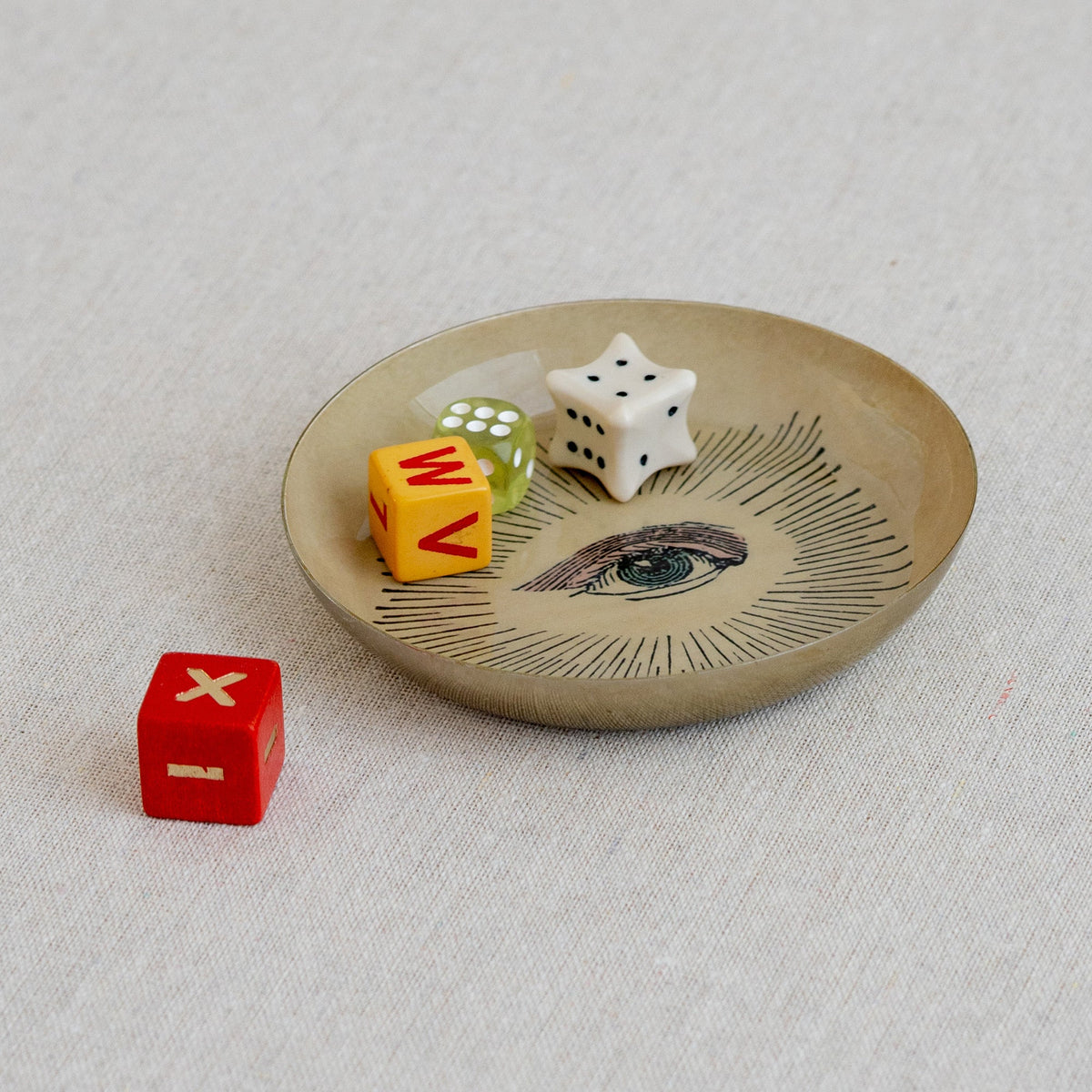Roomytown Round Enamel Tray with an eye design, holding colorful dice, on a light fabric surface.