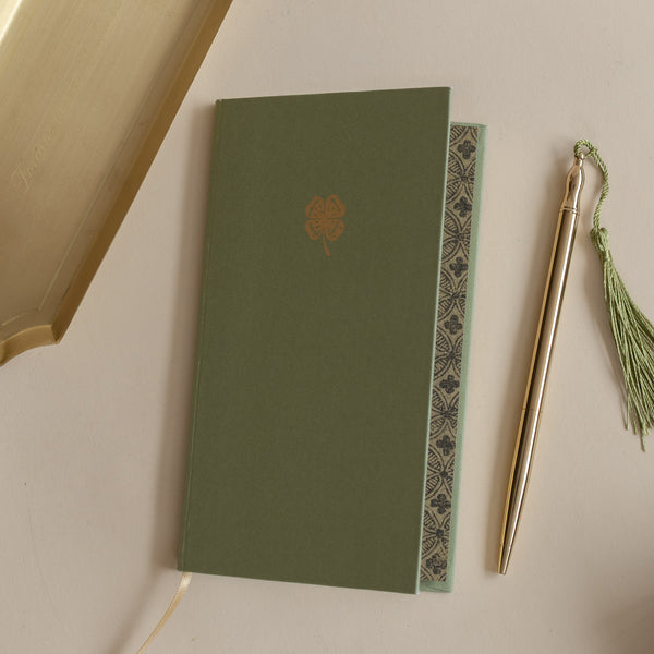Roomytown Slim Lined Notebook with a green cover and gold four-leaf clover, shown with a golden pen and tray.
